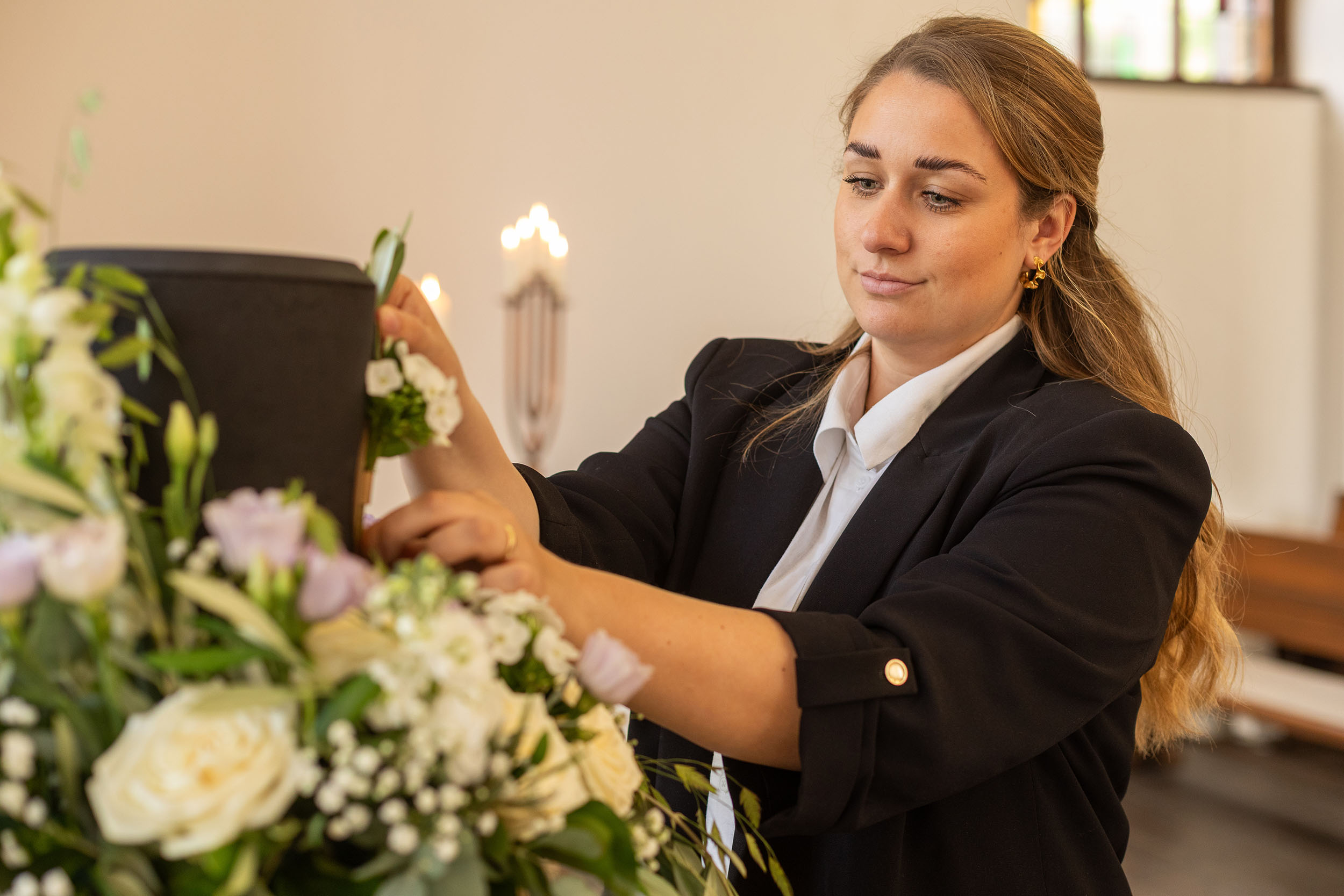 Mitarbeiterin richtet Blumenschmuck an einer Urne für eine persönliche Trauerfeier aus